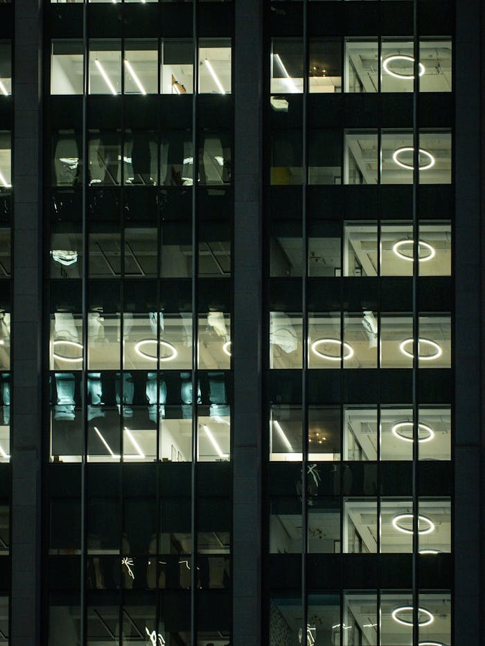 Vertical shot of a modern glass skyscraper at night, showcasing illuminated office windows.